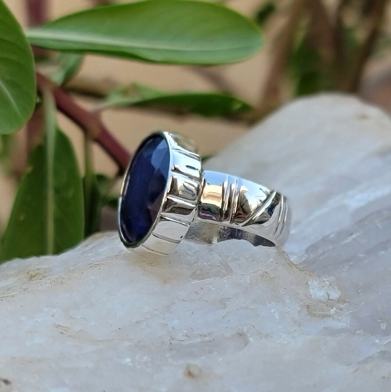May include: A silver ring with a deep blue oval gemstone set in a textured band.