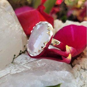 May include: A silver ring with a large, oval-shaped, clear, white gemstone. The ring has a decorative, pointed, silver band.