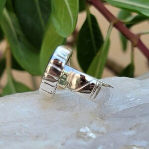 May include: Silver ring with a blue gemstone set in a bezel setting. The ring band is textured and has a polished finish.
