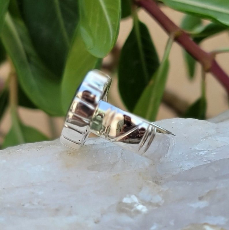 May include: Silver ring with a blue gemstone set in a bezel setting. The ring band is textured and has a polished finish.