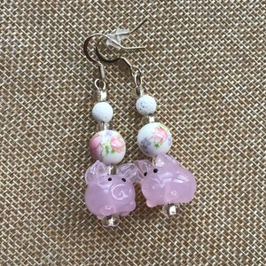 Può includere: Orecchini con ciondolo a forma di maialino rosa, perline floreali bianche e perline di lava bianca.