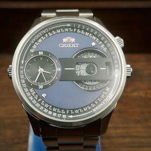 Könnte beinhalten: Eine Orient-Uhr aus Edelstahl mit blauem Zifferblatt und mehreren Hilfszifferblättern. Die Uhr verfügt über eine Kalenderfunktion und ein schwarzes Zifferblatt mit weißen Zeigern. Das Armband der Uhr ist ebenfalls aus Edelstahl.