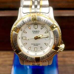 May include: A Casio Quartz watch with a silver and gold-tone stainless steel band and bezel. The watch face is white with black numerals and hands, and the text "CASIO QUARTZ WATER RESIST 30BAR" is visible.