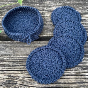 May include: A set of dark navy blue crochet items consisting of one small circular basket with a short decorative tie and four matching circular coasters. Each piece is crafted with a consistent yarn texture and a dense, uniform stitch pattern.