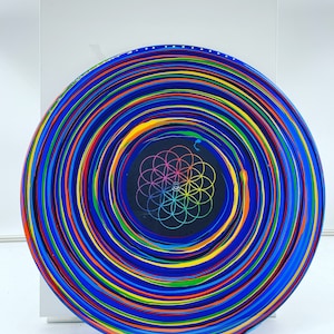 May include: A blue vinyl record with colorful concentric circles and a black center featuring a geometric design. The record is a unique piece of art.