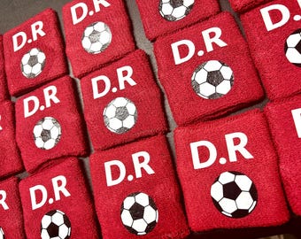 May include: Red wristbands with white lettering that says "D.R." and a white soccer ball graphic.