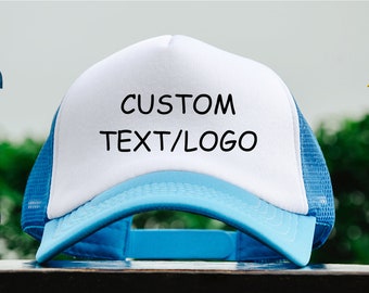 May include: A white trucker hat with a blue brim and mesh back. The hat features the text "CUSTOM TEXT/LOGO" in black. Additional hats in pink, blue, black, red, yellow and green are displayed in the background.