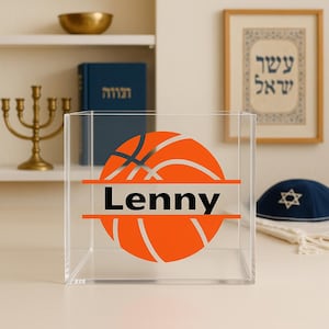 May include: Clear acrylic box with an orange basketball graphic and the name "Lenny" in black. The box is on a white surface, with a menorah, books, and framed artwork in the background.
