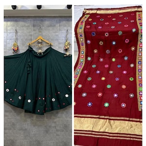 May include: A dark green flared skirt with scattered circular mirror embellishments along the hem and a matching deep red fabric piece featuring colourful embroidered floral motifs with mirrors and gold-toned horizontal border stripes.