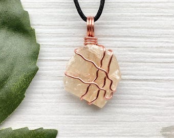 May include: A delicate copper wire wrapped pendant featuring a clear, light brown crystal. The pendant hangs from a black cord.