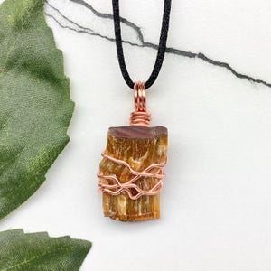 May include: A copper wire wrapped tiger's eye pendant necklace with a black cord. The pendant is a natural, raw, brown and gold tiger's eye stone.
