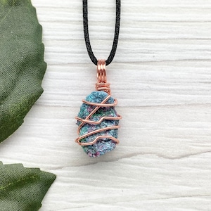 May include: A copper wire wrapped pendant featuring a blue, green, and purple stone. The pendant is hanging from a black cord.