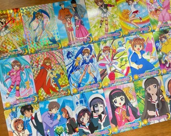 May include: A collection of colorful trading cards featuring anime characters. The cards showcase various characters in action poses, with vibrant backgrounds and holographic foil accents. The text "CARD CAPTOR SAKURA" is visible on the cards.