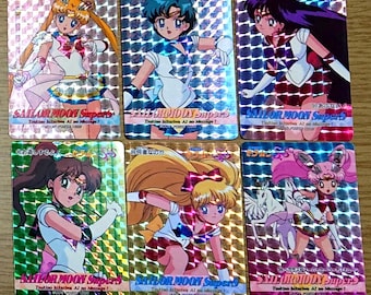 May include: Six rectangular Sailor Moon SuperS trading cards with a holographic grid pattern. Each card features a different anime character in a sailor-style uniform, with the text Sailor Moon SuperS printed at the bottom of each card.