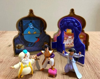 May include: A set of three plastic character figurines including a bearded sultan in white and gold, a male figure in purple and white holding a sword, and a female figure in a light blue outfit, displayed before a gold and blue folding palace playset.