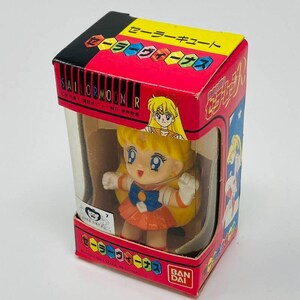 Op de afbeelding: Een Sailor Moon R-figuur in een doos. Het figuur is een stripfiguur met geel haar, een oranje rok en witte handschoenen. De doos is rood met Japanse tekst en een doorzichtig plastic venster.