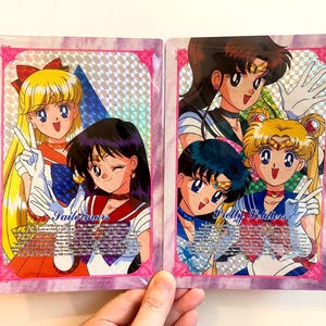 May include: Two trading cards featuring anime characters. The cards have a pink border with a holographic background. One card has the text "Sailorwars" and the other has "Pretty Soldiers". The characters are in colorful outfits.