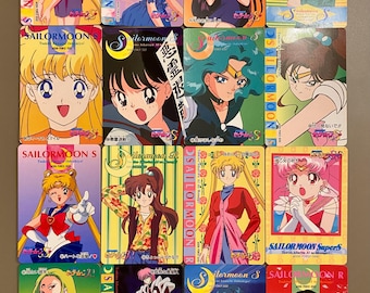 May include: A collection of sixteen rectangular Sailor Moon trading cards featuring various anime characters in colorful outfits, with Japanese text, series logos, and character illustrations displayed in a four-by-four grid layout.