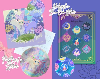 Puede incluir: Un conjunto de papelería que incluye una postal cuadrada con dos gatos, una pegatina holográfica circular con un gato y una hoja rectangular de pegatinas del equipo Sailor Moon con varios símbolos mágicos en tonos morados y dorados.