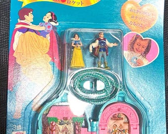 Puede incluir: Un juego de juguetes de Blancanieves y los Siete Enanitos en su embalaje original. El embalaje es de color verde azulado y presenta ilustraciones de Blancanieves, el Príncipe y los Siete Enanitos. El juego incluye figuras en miniatura y una casita.