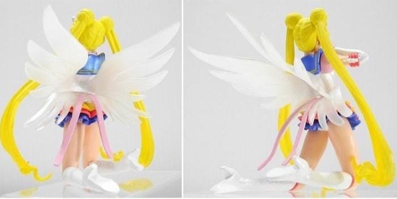 May include: A Sailor Moon figurine featuring long yellow pigtails, large translucent white wings, and a blue and white sailor-style outfit with a pleated skirt. The character is depicted in a kneeling position with white boots and pink ribbons.