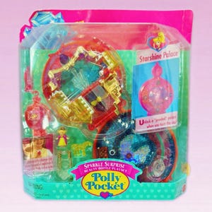 Może przedstawiać: Zestaw Polly Pocket Sparkle Surprise Beauty Bottle Playset w stylu vintage w oryginalnym opakowaniu. Zestaw zawiera miniaturowy pałac, figurki i akcesoria. Opakowanie jest różowe, niebieskie i z przezroczystego plastiku, z napisem "Starshine Palace".