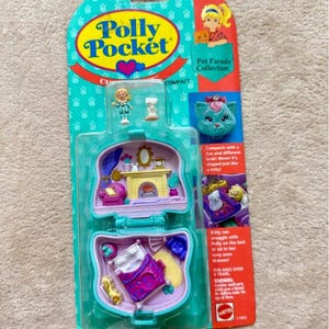 Puede incluir: Un juguete compacto vintage de la colección Polly Pocket Pet Parade. La caja de plástico turquesa se abre para revelar una escena de dormitorio en miniatura con una cama, muebles y una pequeña figura de Polly Pocket. El embalaje presenta un diseño en forma de gato y el logotipo de Polly Pocket.