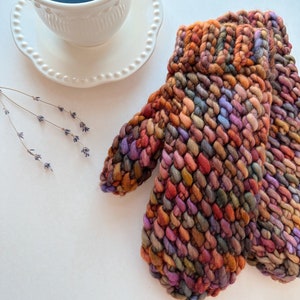 K&ouml;nnte beinhalten: Ein Paar bunte Strickhandschuhe mit einem strukturierten Muster. Die Handschuhe sind aus verschiedenen Braunt&ouml;nen, Orange, Lila und Gr&uuml;n gefertigt.