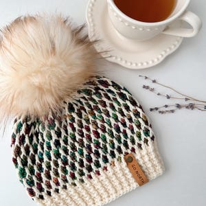May include: A white and green crocheted beanie with a faux fur pom pom and a brown leather patch that says "GO NORTH".