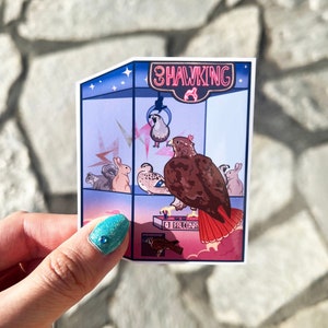May include: A sticker featuring a cartoon illustration of a claw machine labeled "3 Hawking". The machine contains various birds and small animals. The hawk is brown and red. The background is a gradient of pink and blue.