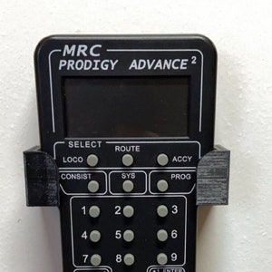 Könnte beinhalten: Ein schwarzer MRC Prodigy Advance 2 Modellbahnregler mit einem digitalen Display und einer Vielzahl von Tasten und Knöpfen. Der Regler hat ein schwarzes Kunststoffgehäuse und einen silbernen Metallknopf.