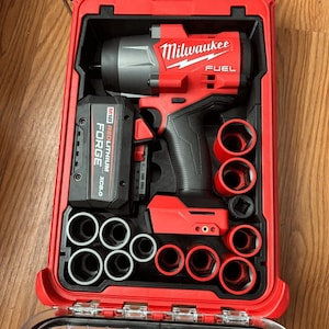May include: A red Milwaukee FUEL impact wrench kit in a red carrying case. The kit includes the impact wrench, battery, and various sockets. The case is open, revealing the tools neatly organized inside. The text "Milwaukee" and "FUEL" are visible.