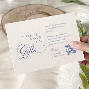 Puede incluir: Una tarjeta de regalo de boda color crema con una elegante escritura azul que dice "A Simple Note on Gifts". La tarjeta incluye un código QR y los nombres Charlotte & Matthew. La tarjeta es sostenida por una mano.