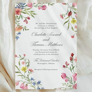 May include: A wedding invitation with floral watercolor accents. The invitation features the names Charlotte Seward and Thomas Matthews, with event details. The design includes pink, yellow, and blue flowers, and green leaves.