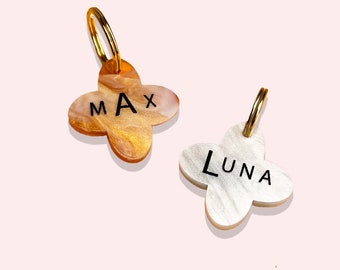 May include: Two gold and silver dog tags in the shape of a four-leaf clover. The gold tag says "MAX" and the silver tag says "LUNA".