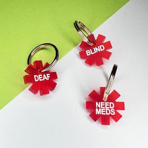 May include: Three red star-shaped keychains with white text. The keychains read "DEAF", "BLIND", and "NEED MEDS".