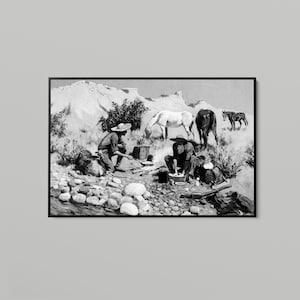 May include: A black and white framed print depicting a western scene with two figures cooking over an open fire in a rocky landscape. Three horses stand in the background near a mountain range. The artwork features detailed shading and textures.