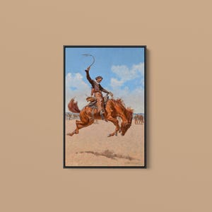Könnte beinhalten: Ein gerahmtes Gemälde, das einen Cowboy auf einem bockenden braunen Pferd in einer staubigen Arena unter blauem Himmel zeigt. Der Reiter trägt einen Hut und Chaps und hält ein Seil hoch in die Luft. Die Szene fängt einen dynamischen Moment ein.