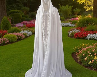 May include: A long, flowing white hooded cloak with a decorative trim down the front. The cloak is displayed on a mannequin in a garden setting with green grass and colorful flowers.