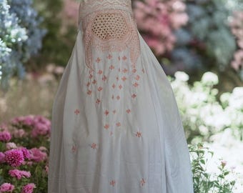 May include: A white burqa with pink embroidery. The burqa has a mesh panel over the face.