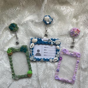 May include: Four decorative badge holders with matching retractable reels. The holders are in green, blue, and purple, and are embellished with seashells, flowers, and small cacti. The badge holders have a clear window for inserting an ID card.
