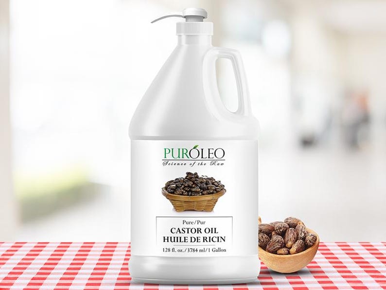 May include: A white plastic jug of castor oil with a pump dispenser. The label reads "PUR&Oacute;LEO Science of the Raw" and "CASTOR OIL HUILE DE RICIN". A small wooden bowl of castor beans sits next to the jug. The jug contains 128 fl. oz. of oil.