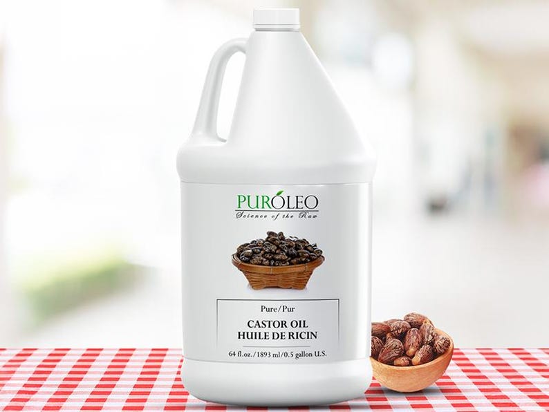 May include: A white plastic jug of castor oil with a handle, labeled "PUR&Oacute;LEO." The label includes text in English and French, and a graphic of castor beans in a wooden bowl. A small wooden bowl of castor beans sits to the right.