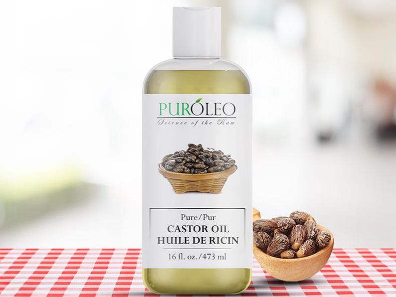 May include: A clear bottle of Puroleo castor oil with a white label featuring a basket of seeds. The label also includes the text "Science of the Raw" and "Pure Castor Oil 16 fl. oz.". A small wooden bowl filled with seeds sits to the right.