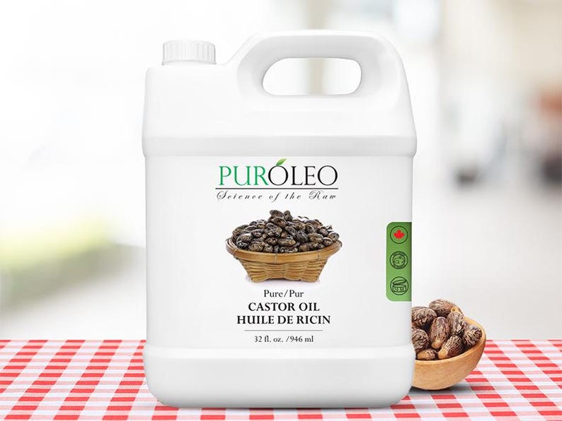 May include: A white plastic jug of PurOleo Castor Oil. The label features a basket of castor beans and the text "Pure/Pur Castor Oil Huile de Ricin 32 fl. oz. / 946 ml." A small wooden bowl of castor beans sits to the right.