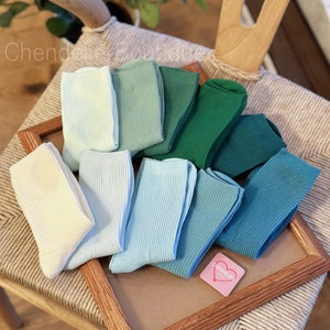 May include: A collection of ten pairs of socks in various shades of blue and green. The socks are arranged in a gradient pattern, with the lightest shade of blue at the top and the darkest shade of green at the bottom. The socks are made of a soft, comfortable material and are perfect for everyday wear.