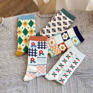 May include: Five pairs of colorful socks with different patterns. The socks feature geometric designs, flowers, and smiley faces.