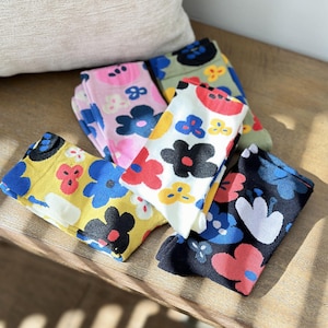 May include: Five pairs of colorful socks with floral patterns. The socks are in various colors, including yellow, blue, pink, white, black, and green. The flowers are large and abstract, with different shapes and sizes.