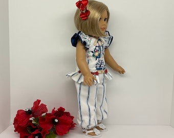 May include: A doll wearing a white and blue striped pants with a white top with a blue and white floral print and red bow hair clips. The doll is wearing white sandals.
