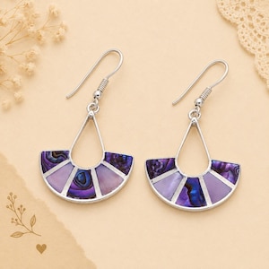 Könnte beinhalten: Ein Paar silberfarbene Ohrhänger mit fächerförmigem Design. Jeder Ohrring ist mit abwechselnden Segmenten aus irisierendem violettem Abalone-Muschelmaterial und glattem, hellviolettem Stein eingelegt und an einem einfachen Silberhaken befestigt.